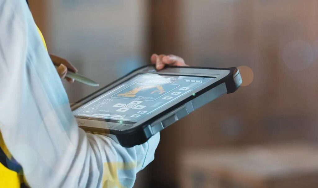 Worker in a safety vest uses a rugged tablet with a stylus to view controls.
