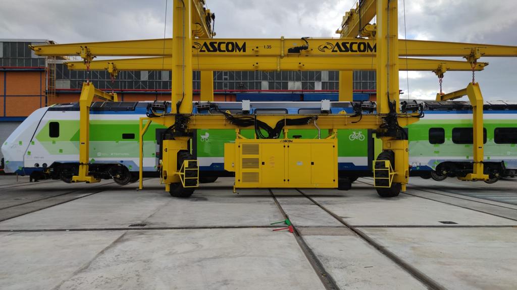 Yellow railway maintenance gantry over a green-and-white passenger train in a depot yard.